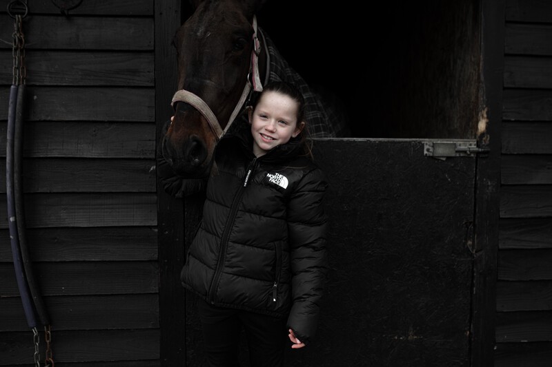 Alice standing with a brown horse in it's stable