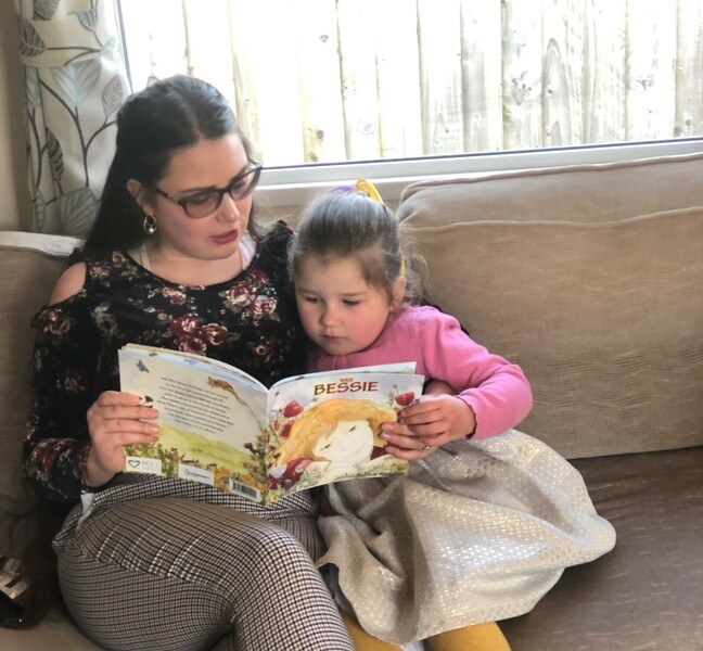 Woman reading book to young girl on sofa