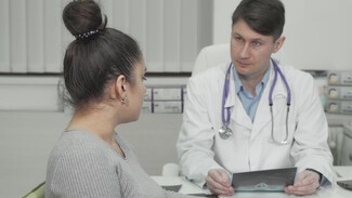 A youngwoman with brown hair in a high bun talks to a doctor