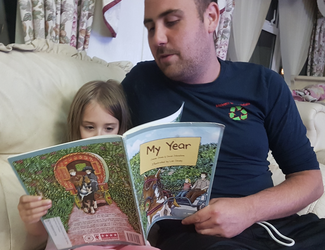 Young girl reading book with her dad sat on the sofa 
