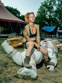 young woman in shorts and sports bra and high-vis, sitting on large sculpture of a baby