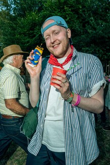 A young white man smiling wearing blue and white shirt and red neckerchief and clue cap