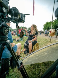 young white woman with blonde hair and black long dress sitting in front of video camera