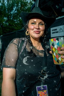 white woman wearing black mesh stop and black hat holding plastic cup