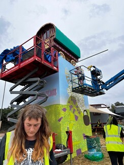 worker in high-vis with crane and platform with a Romany bowtop wagon on top