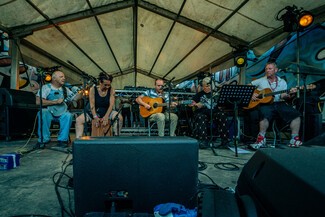 A group of musicians with guitars and percussion instruments playing sitting down on a stage 